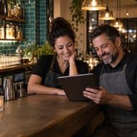 An owner and a server looking at a tablet at the bar